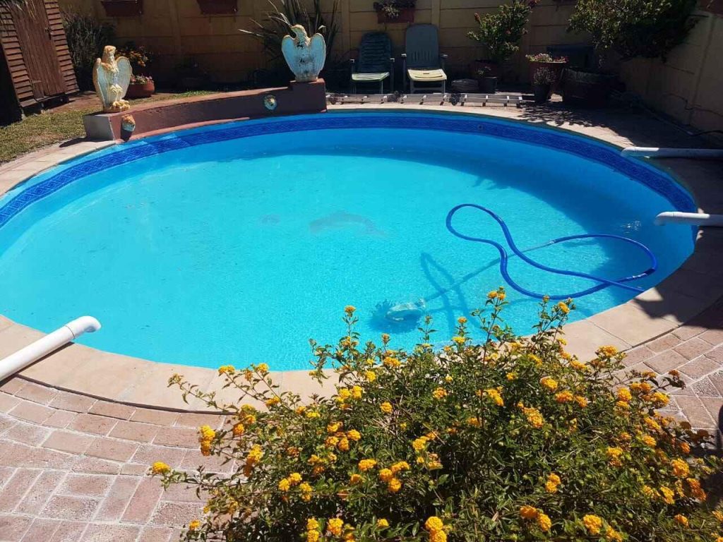 Round pool edged with sandstone-coloured coping that blends into clay brick paving