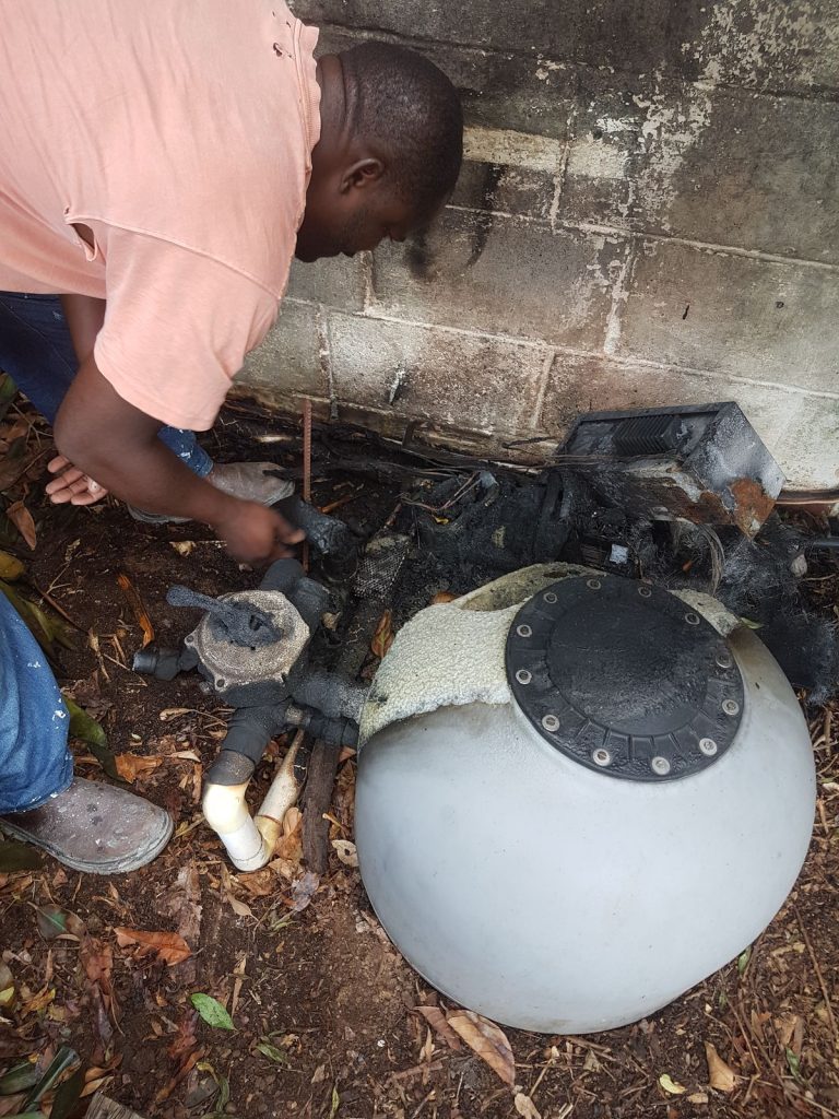 Technician reworking the pump and filter plumbing at ground level beside a sand filter