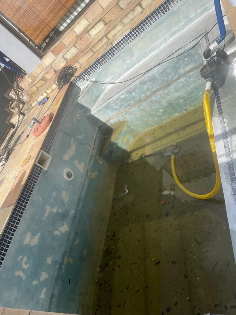 Faded and worn fibreglass swimming pool with visible surface cracks and discolouration before professional relining service.