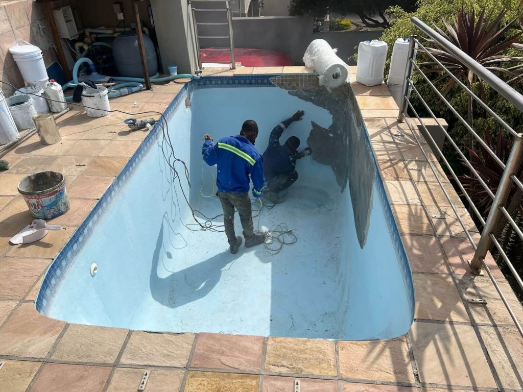 Mid-renovation image showing fibreglass being applied to a swimming pool surface by expert technicians, part of a professional pool relining project.