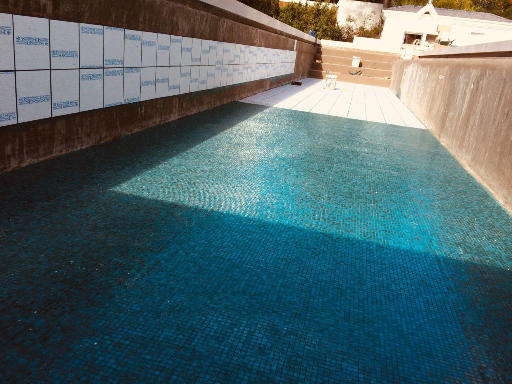 Technicians installing ceramic tiles on the interior surface of a swimming pool during a tiling project, showcasing expert renovation work.