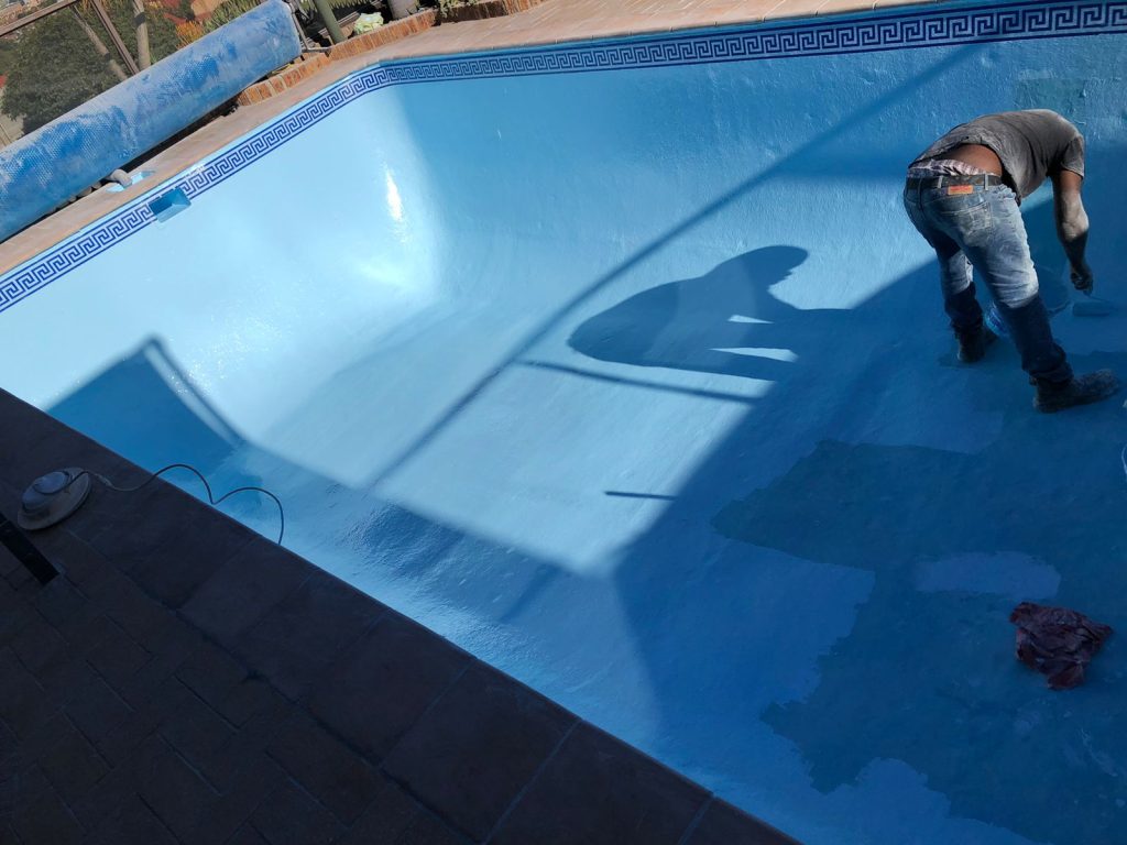 Pool technician painting the inside of a drained fibreglass swimming pool