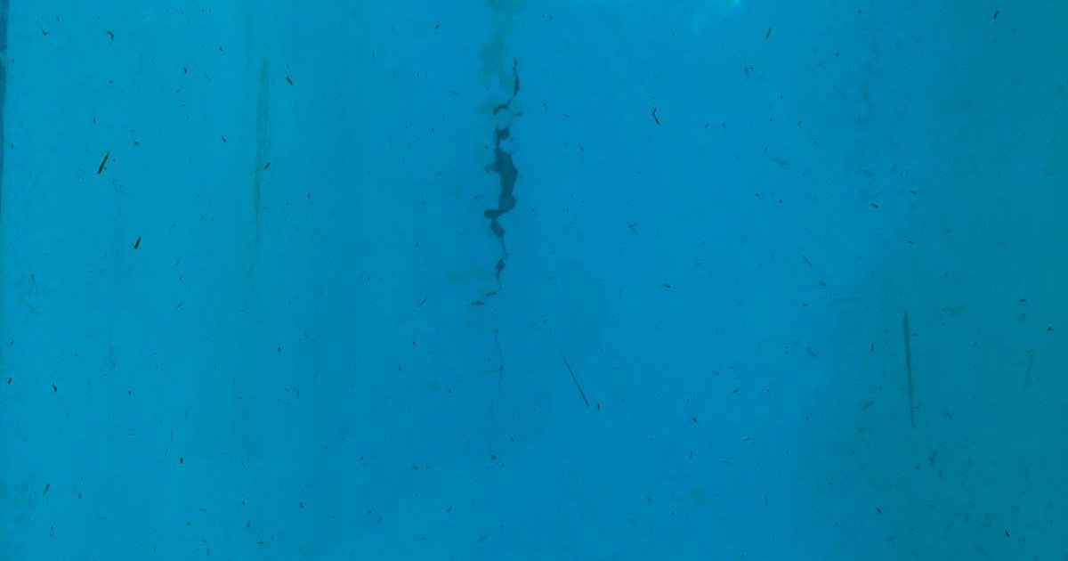 Pool technician inspecting a residential swimming pool for leaks in Cape Town using professional equipment near the waterline, with clear water and visible surface cracks