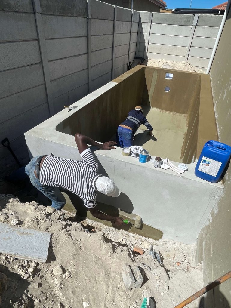 Concrete swimming pool shell being waterproofed using cement additives and reinforced steel during construction in South Africa