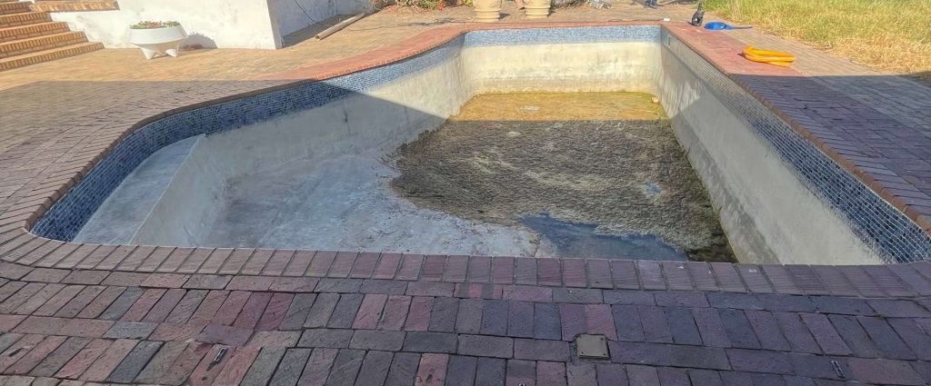 Old marbelite swimming pool with stained surface and black algae growth before fibreglass pool relining in Cape Town