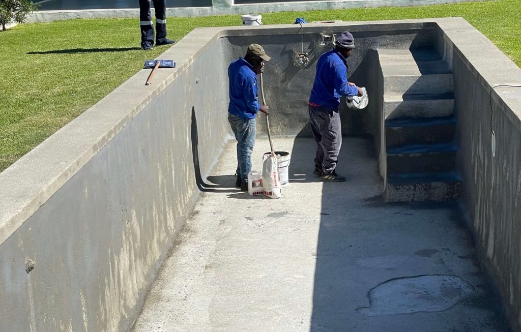Pool renovation team removing damaged marbelite during gunite pool resurfacing process in Yzerfontein