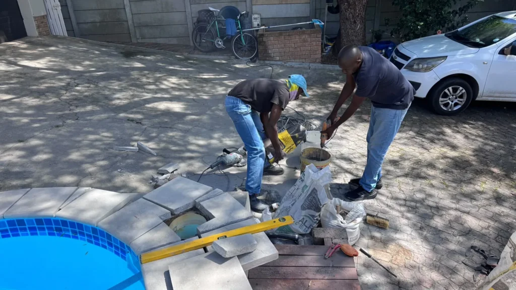 Two team members cutting and preparing coping slabs next to the pool
