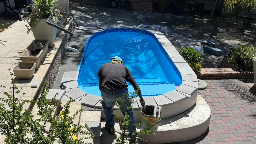 Team member finishing the newly laid copings around the pool with a bucket and brush