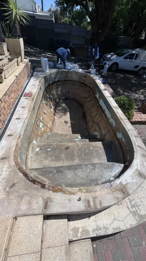 Drained oval pool with the old fibreglass lining stripped back to the bare concrete shell