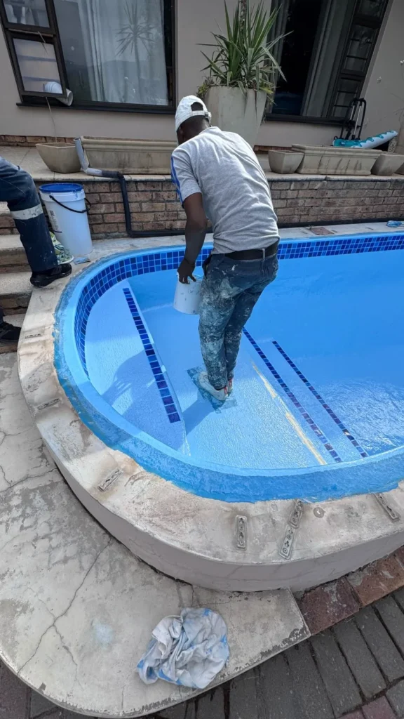 Team member applying the final coat on the pool floor beside the mosaic step markers