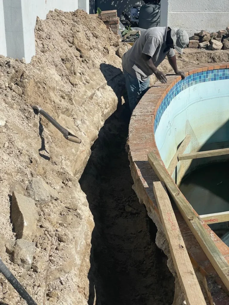 Team member digging a trench along the side of the fibreglass pool shell, with wood purlins bracing the wall
