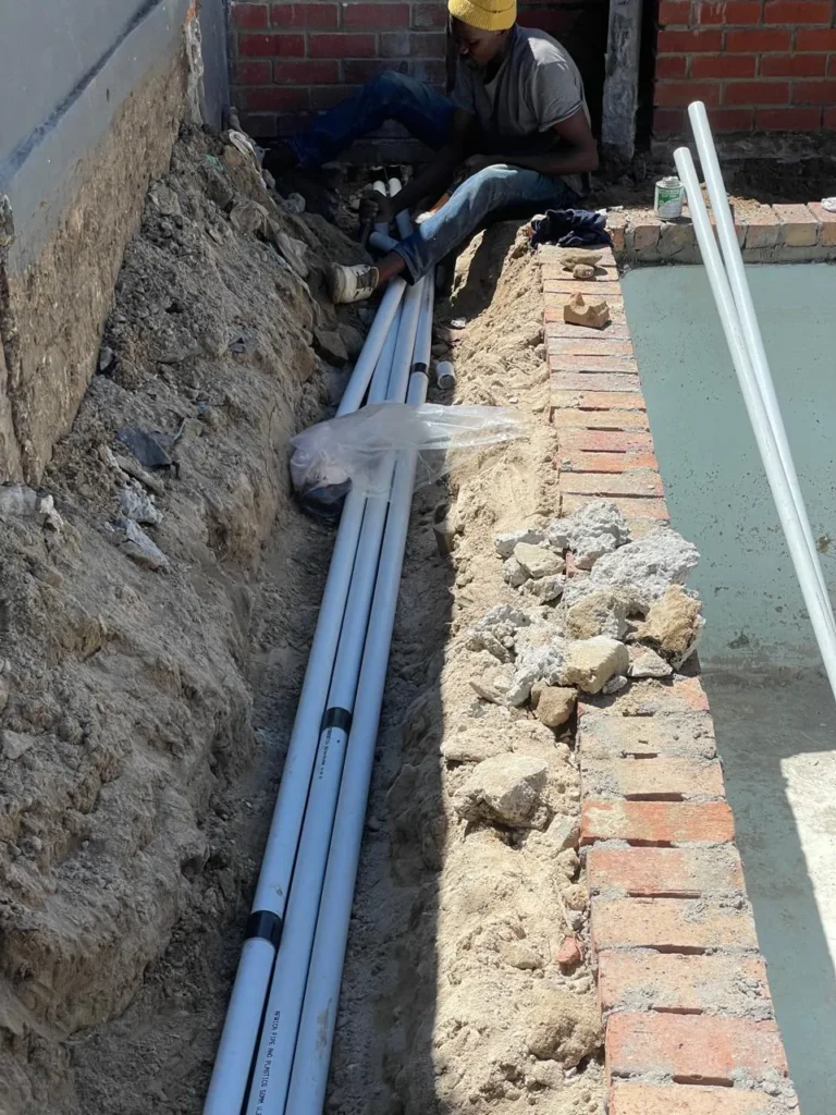 Team member laying pool pipes in a trench beside the pool wall